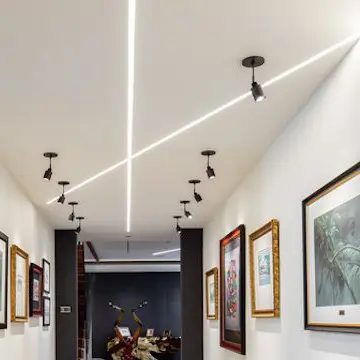 Art gallery hallway with linear LED ceiling lighting and track spotlights on framed paintings