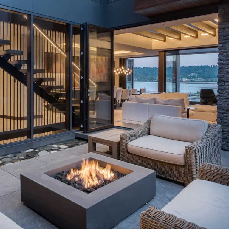 Modern outdoor patio with square fire pit and LED architectural lighting on stairs and glass walls at dusk