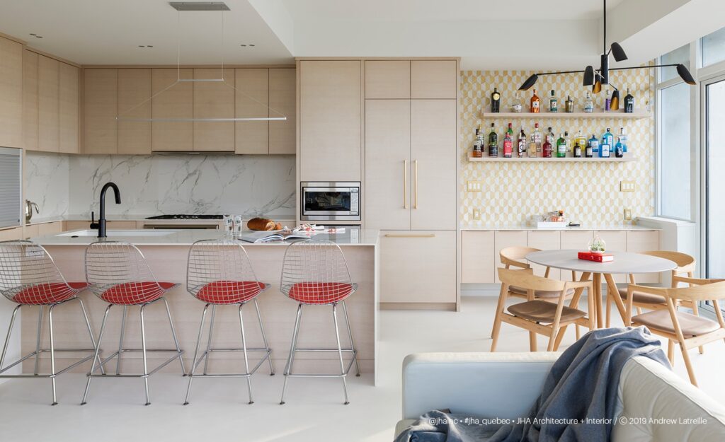 Modern open kitchen with light wood cabinetry, marble island, red wire bar stools, linear LED under-cabinet and ceiling strips, woven accent wall, and large windows